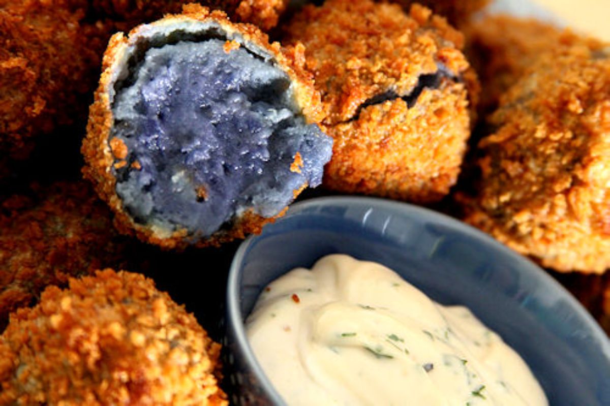Crunch blue potato croquettes with a bowl of dip on a tray.