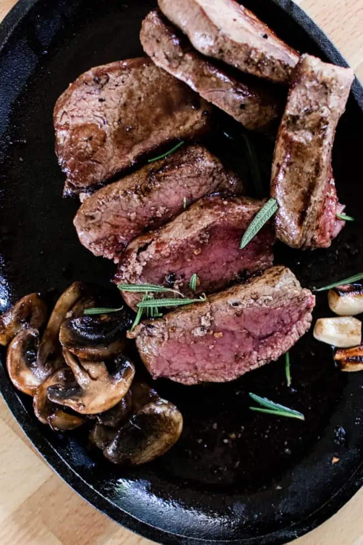 Mouth-watering pan-seared elk steak with sauteed mushrooms and garlic in a black bowl.