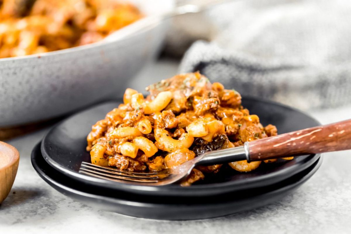 Juicy venison goulash on a black plate with a fork.