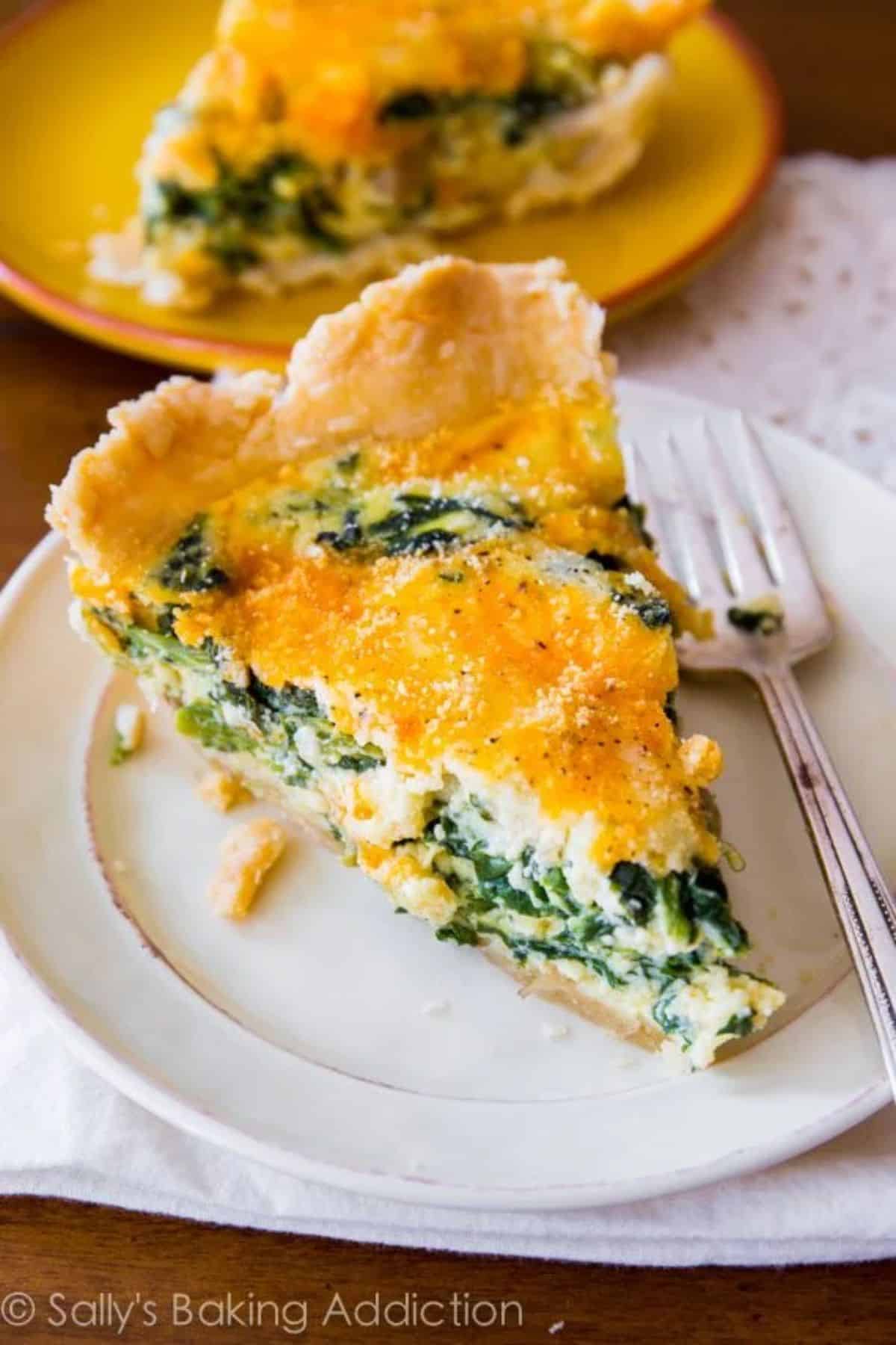 A piece of cheesy spinach quiche on a white plate with a fork.