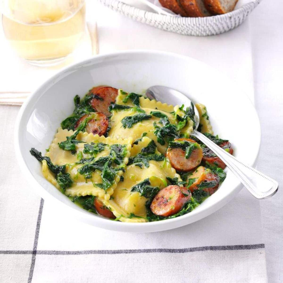 Fresh ravioli with apple chicken sausage in a white bowl with a spoon.