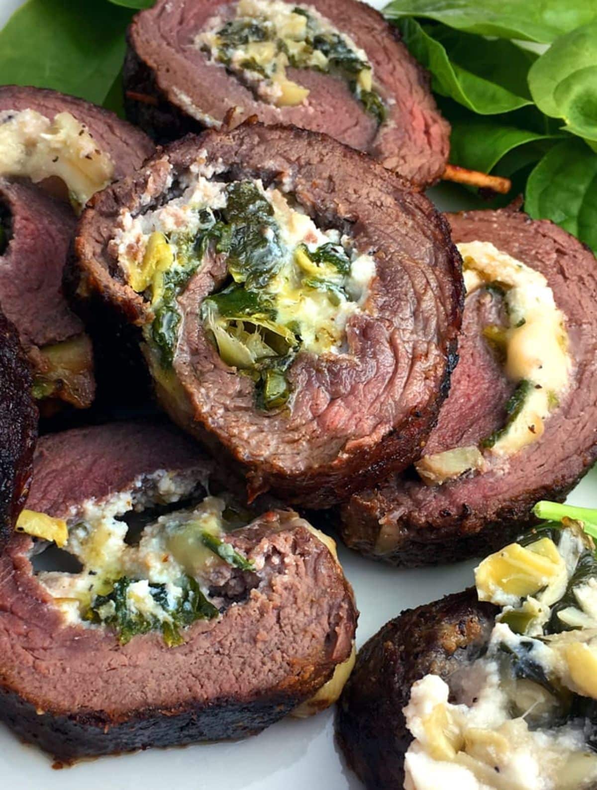 Scrumptious elk steak roulade with artichoke hearts on a white tray.