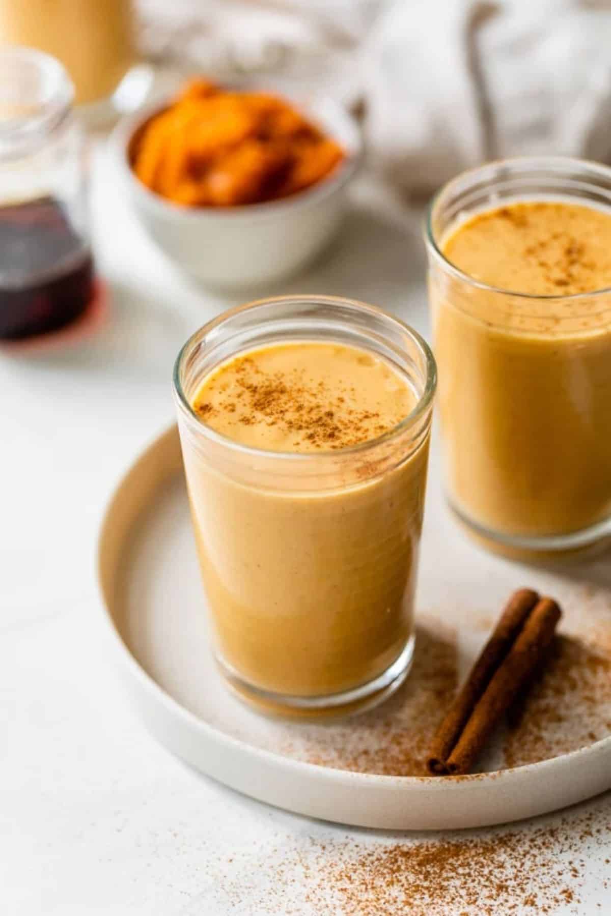 Delicious pumpkin smoothie in two glasses on a tray with cinnamon stick.