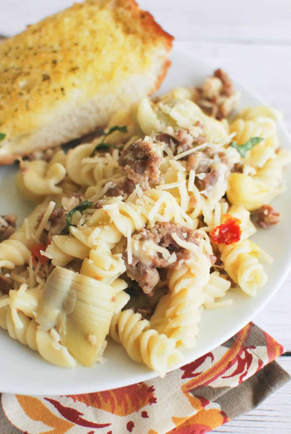 Flavorful pasta with sausage, artichokes, and sun-dried tomatoes on a white plate.