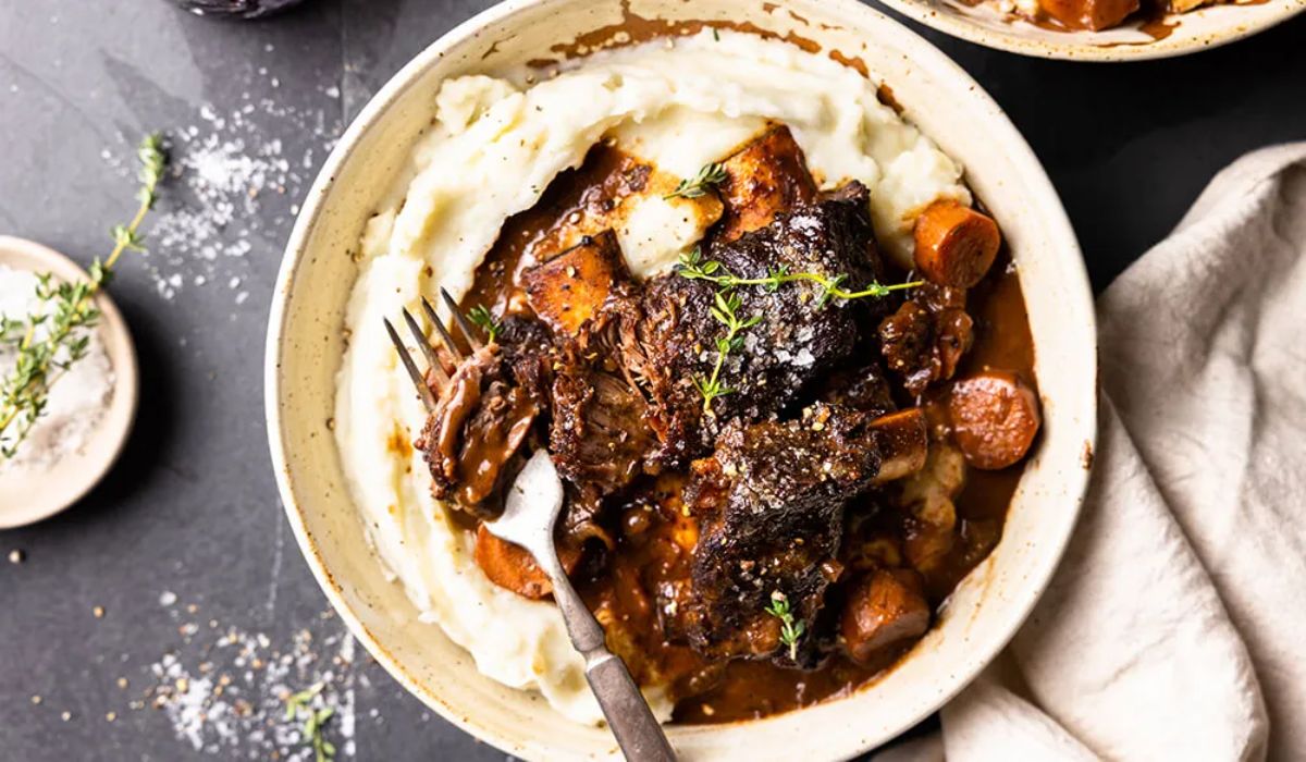 Scrumptious red wine braised bison short ribs with mashed potatoes in a white bowl with a fork.