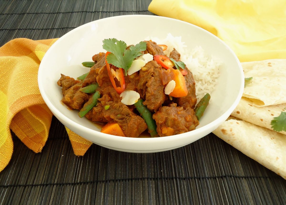 Flavorful beef curry with veggies and rice in a white bowl.