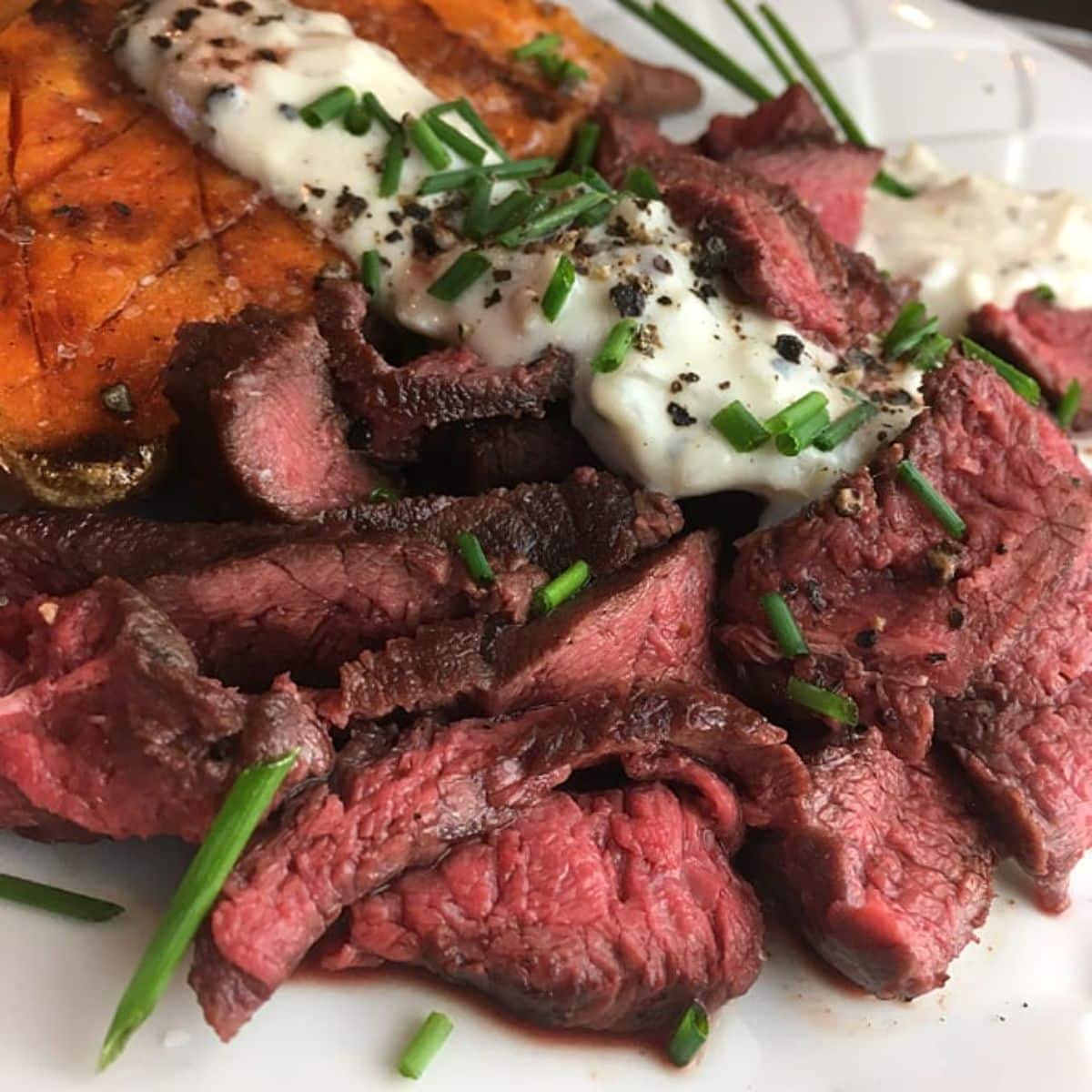 Delicious peppered elk steak with gorgonzola cream sauce on a white tray.