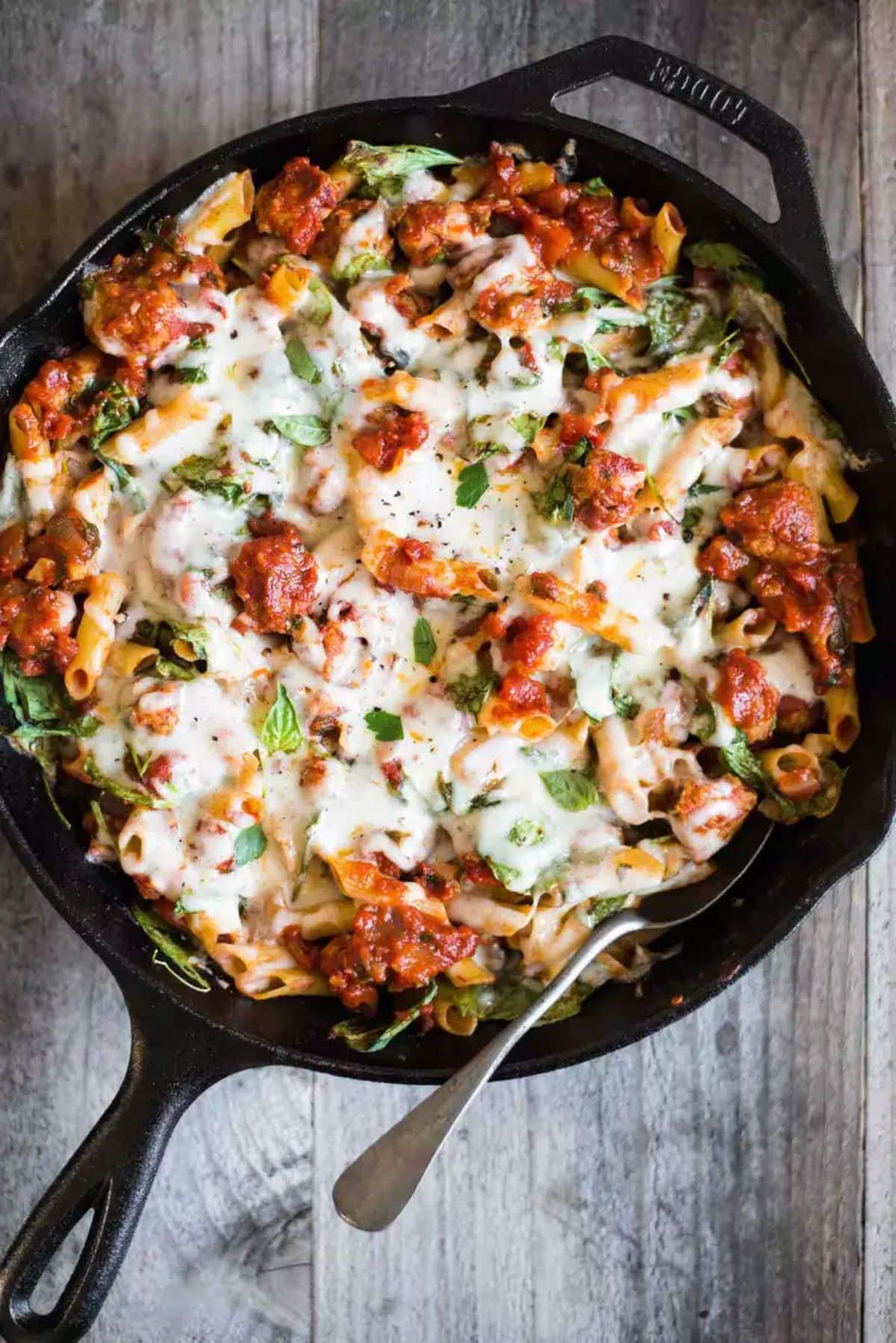 Juicy chicken sausage and pasta in a black skillet.