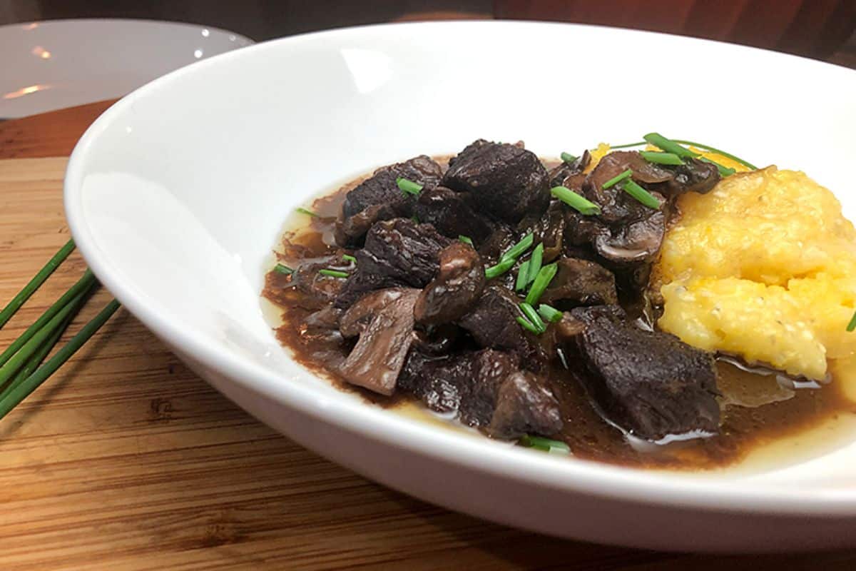 Scrumptious braised elk and mushrooms on a white plate.