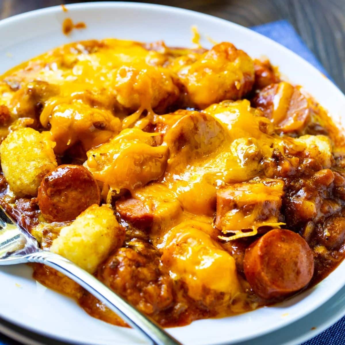 Tasteful cheesy hot dog tater tot casserole on a white plate with a fork.