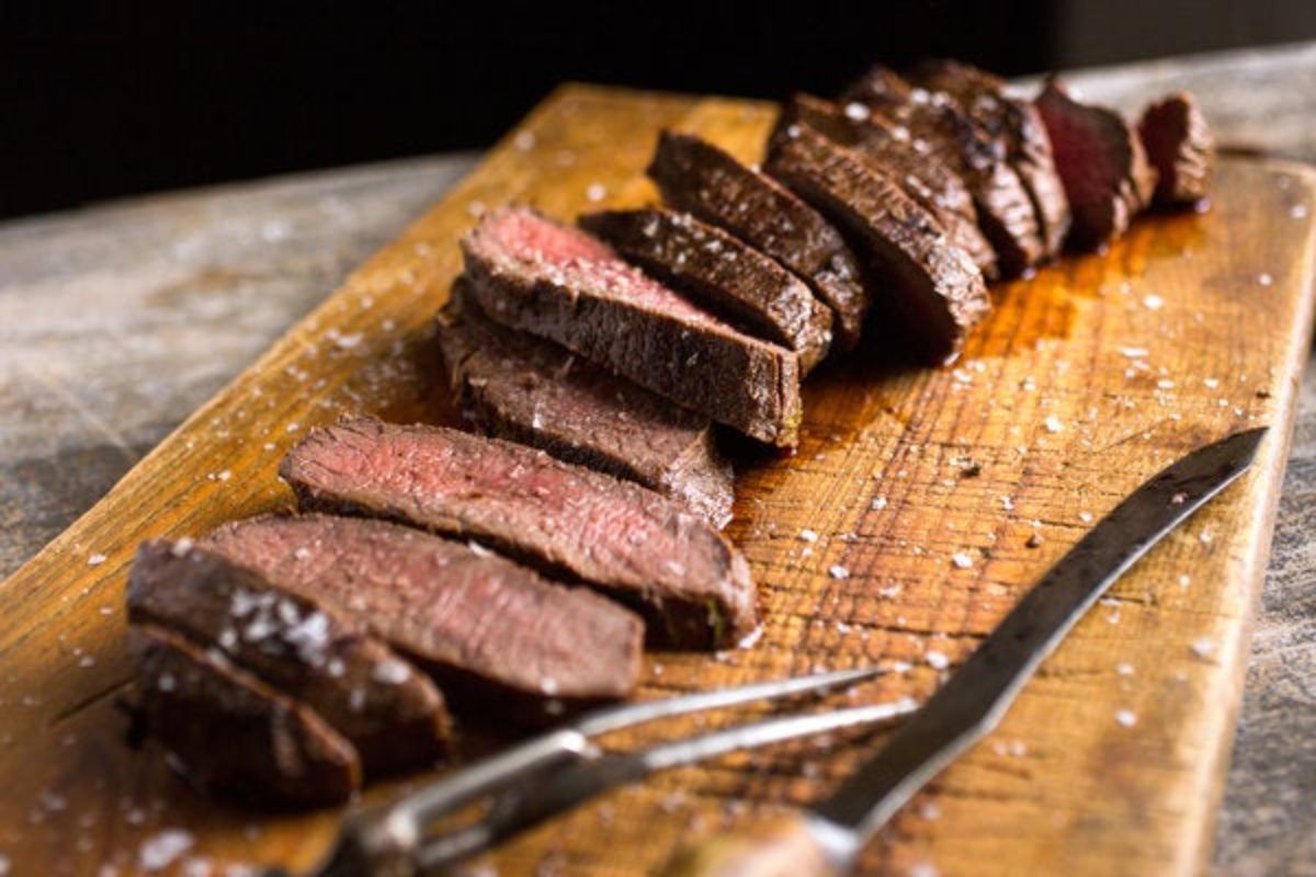 Mouth-watering marinated venison steaks on a wooden tray with cutlery.