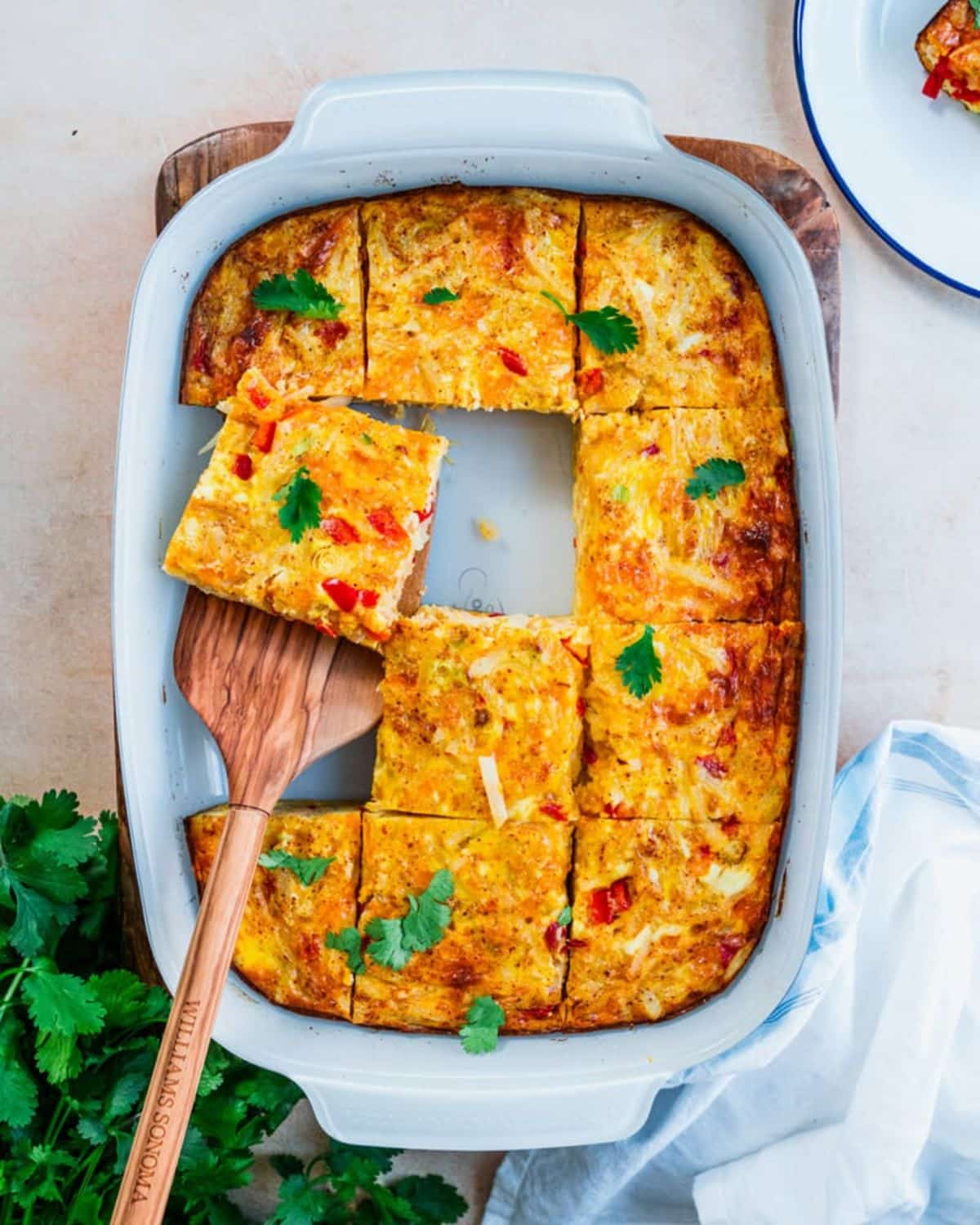 Scrumptious hashbrown breakfast in a blue casserole with a wooden spatula.