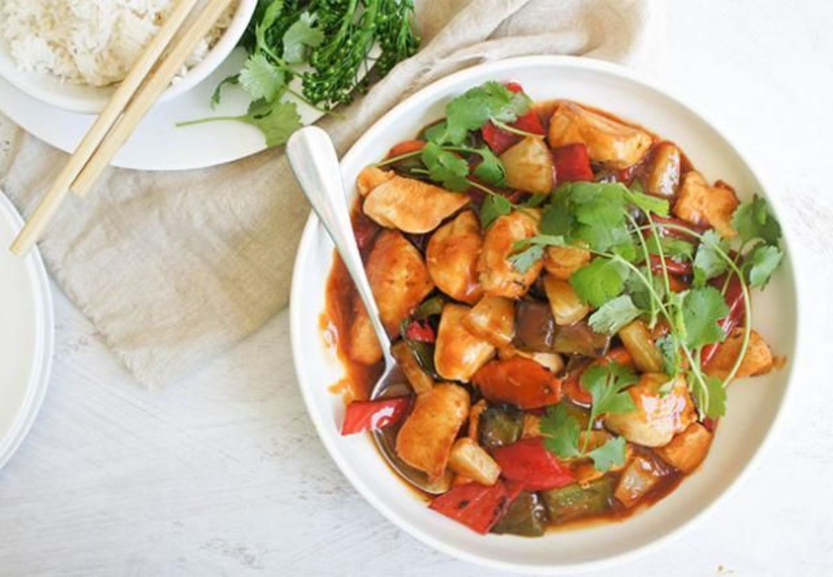 Healthy sweet and sour chicken in a white bowl with a spoon.