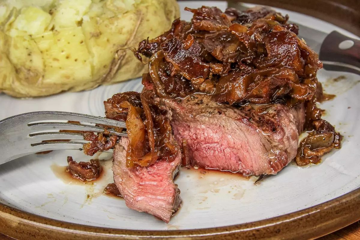 Mouth-. Watering grilled elk steaks with caramelized onion bacon bourbon jam on a tray with cutlery.