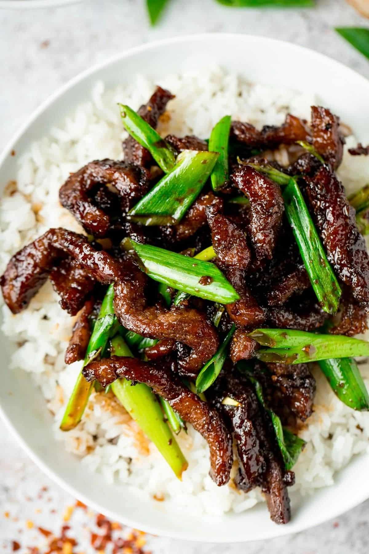 Juicy mongolian beef with veggies and rice in a white bowl.