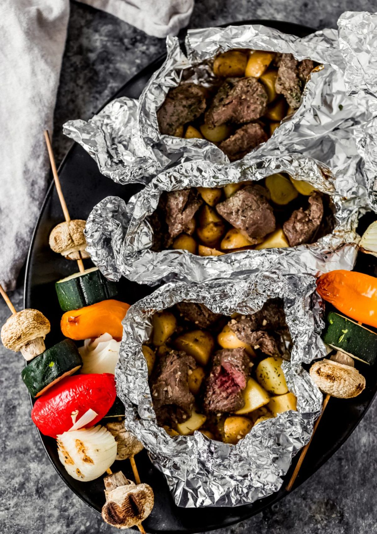Flavorful elk sirloin steak and potato foil packs on a black tray.