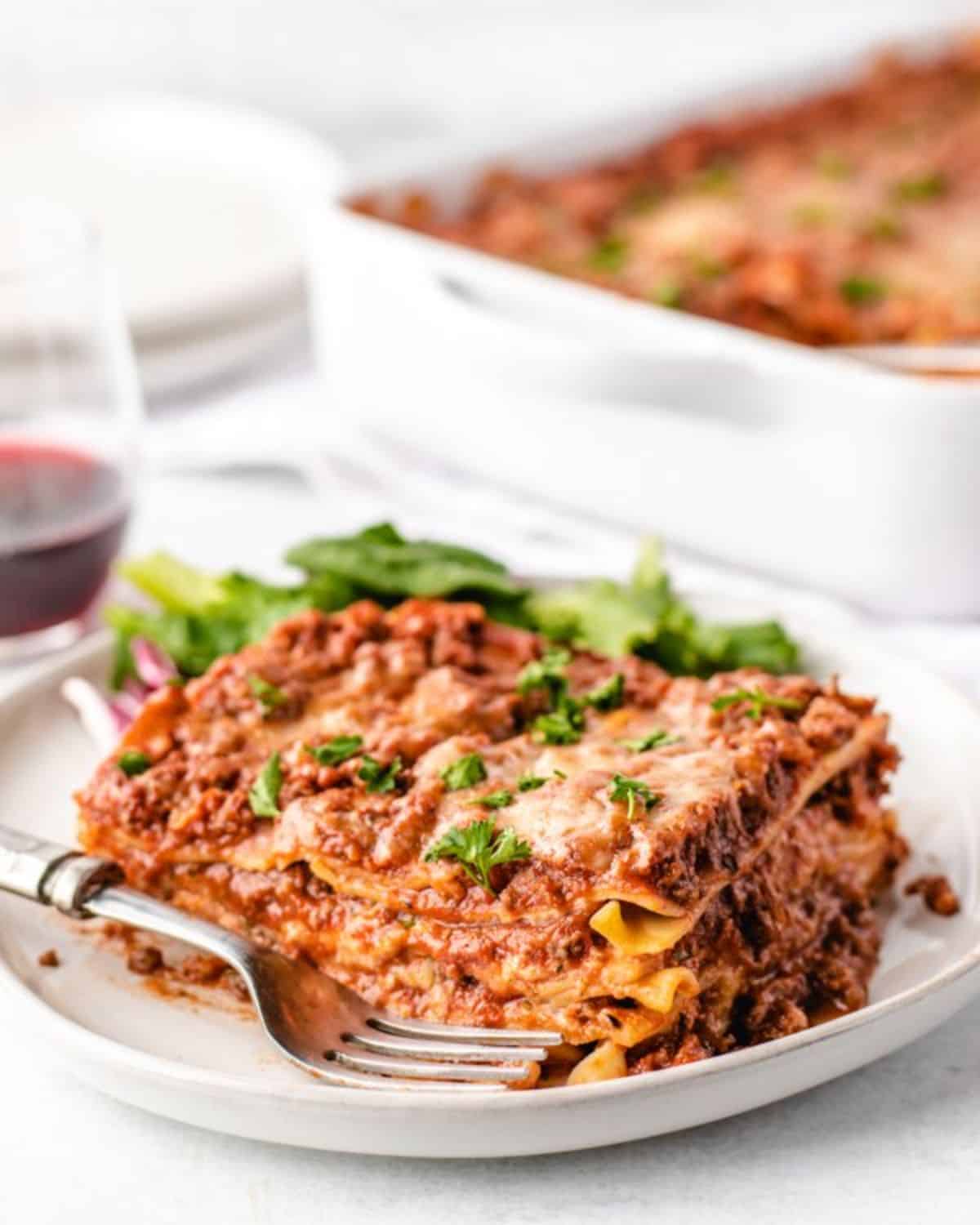 A piece of venison lasagnaon a white plate with a fork.