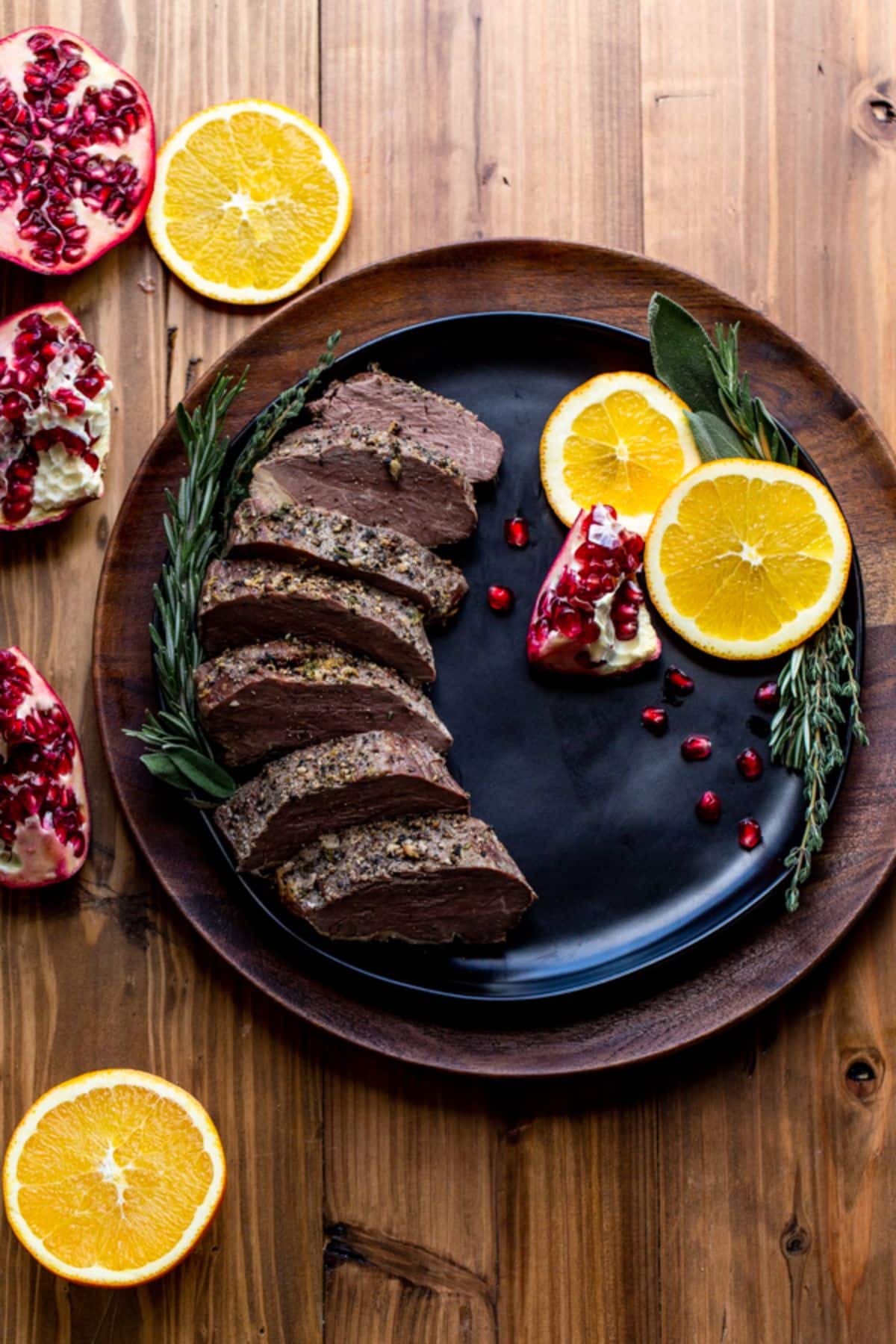 Sliced roasted bison tenderloin with lemon slices on a black plate.