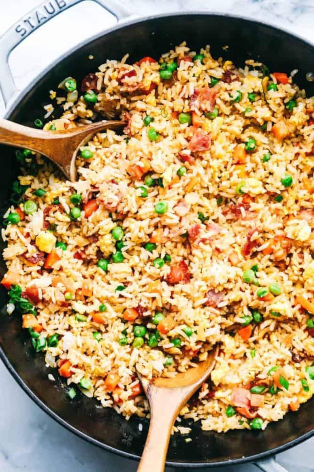 Healthy bacon fried rice in a skillet with two wooden spoons.