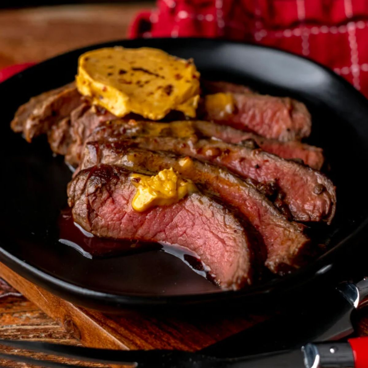 Mouth-watering  elk steak with chipotle compound butter on a black plate.