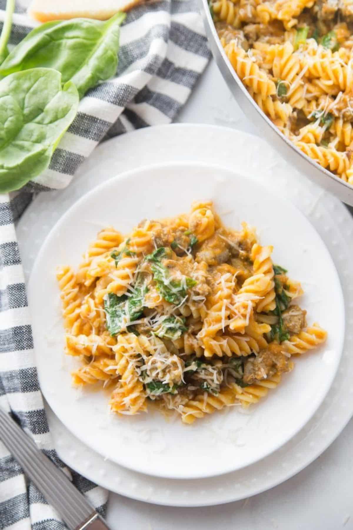 Healthy pumpkin pasta with spicy chicken sausage on a white plate.