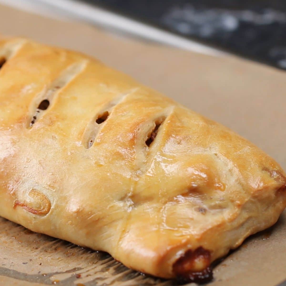 Flavorful sausage, onion, and peppers pizza roll on a tray.