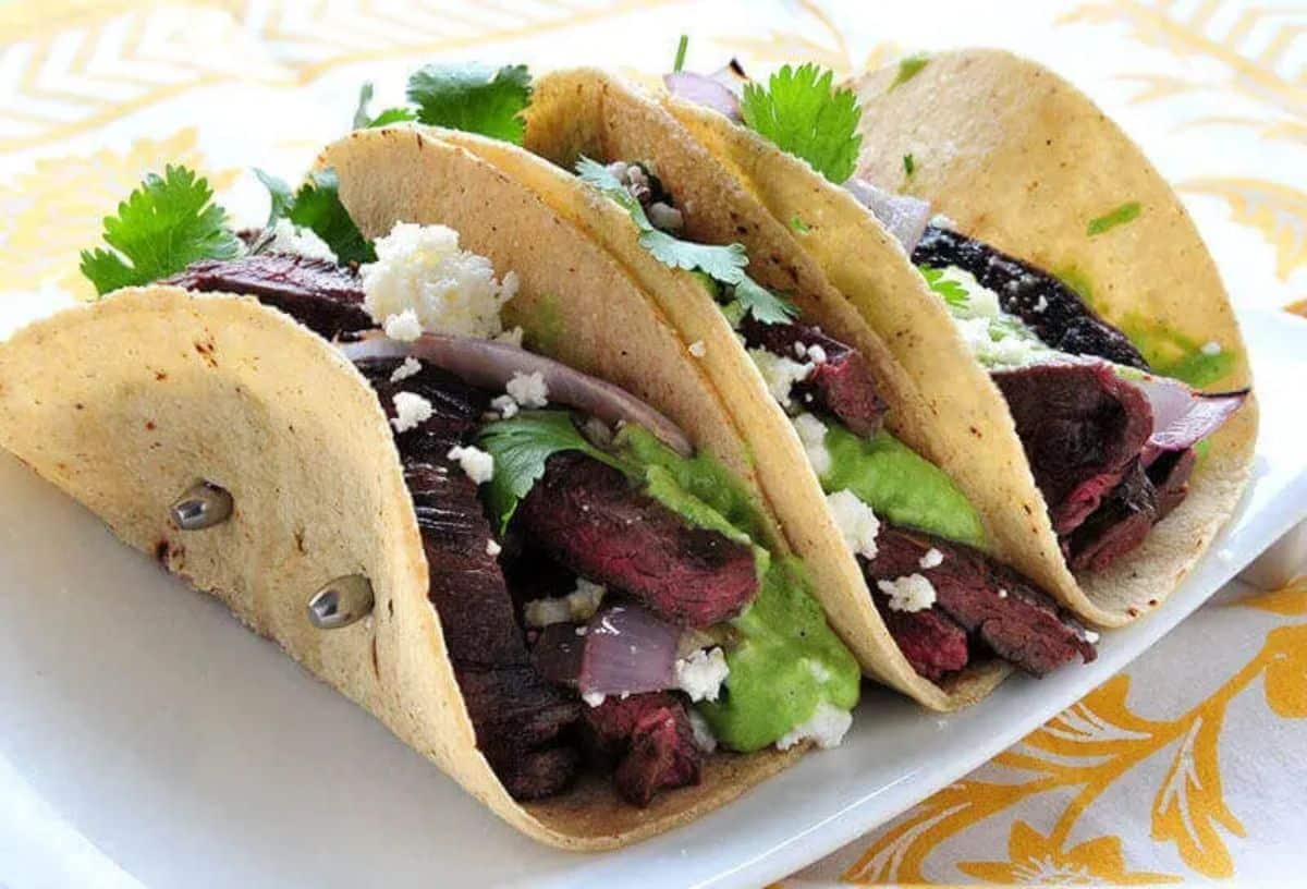 Scrumptious elk skirt steak tacos with tomatillo avocado sauce on a white tray.