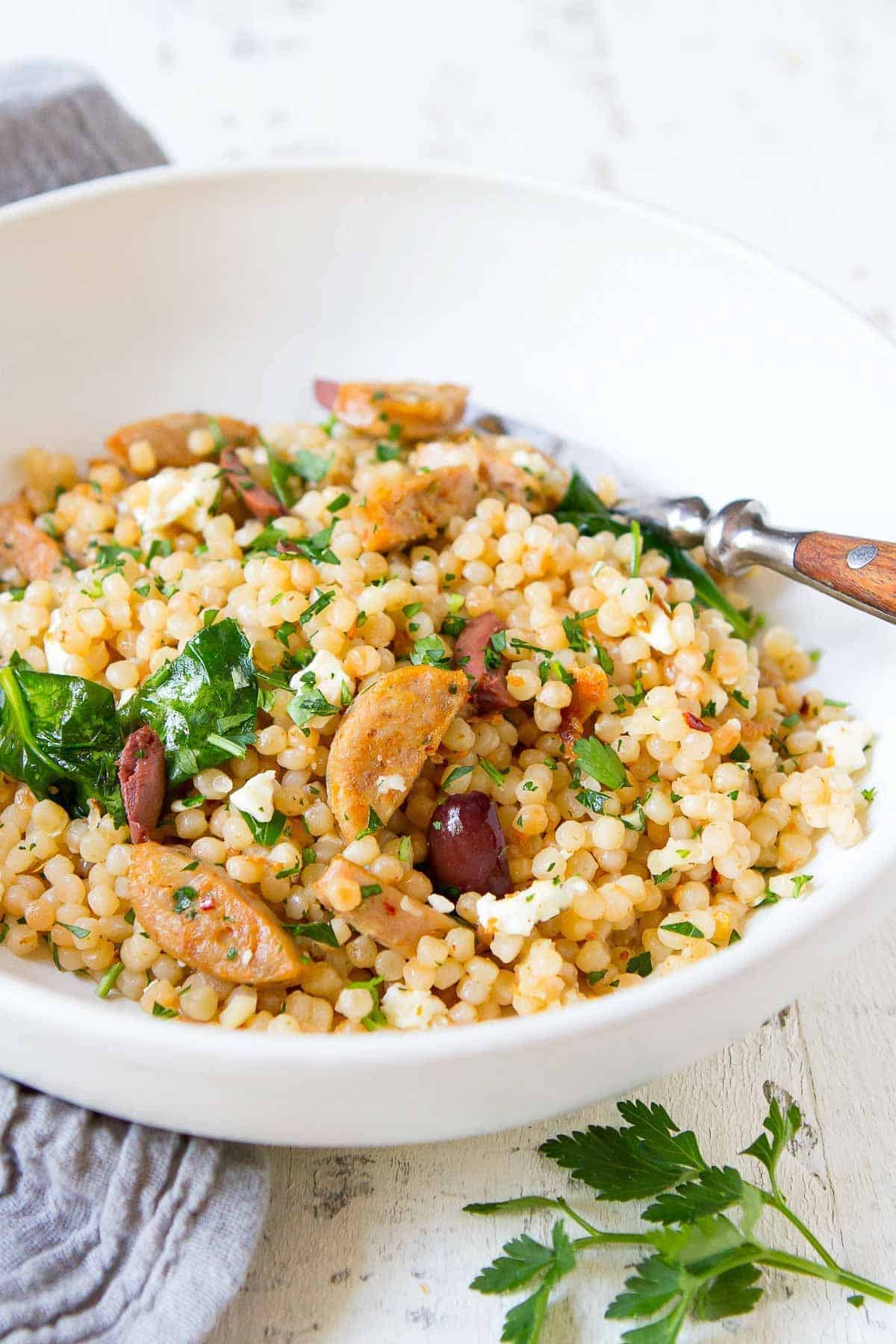 Flavorful israeli couscous in a white bowl with a fork.