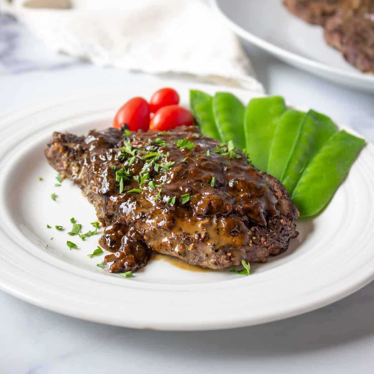 Juicy elk steak au poivre with veggies on a white plate.