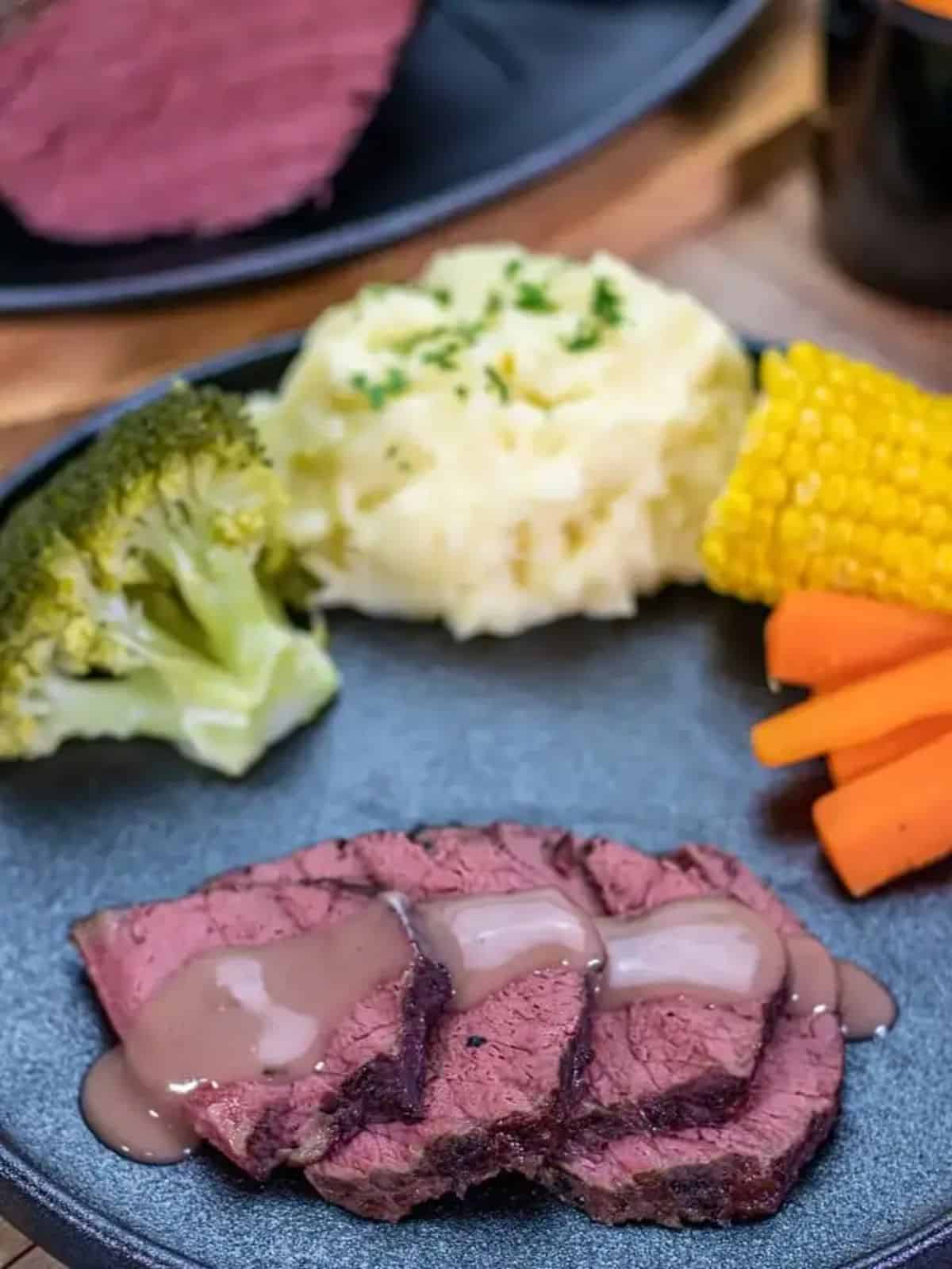 Delicious corned beef in red wine with mashed potatoes and veggies on a gray plate.
