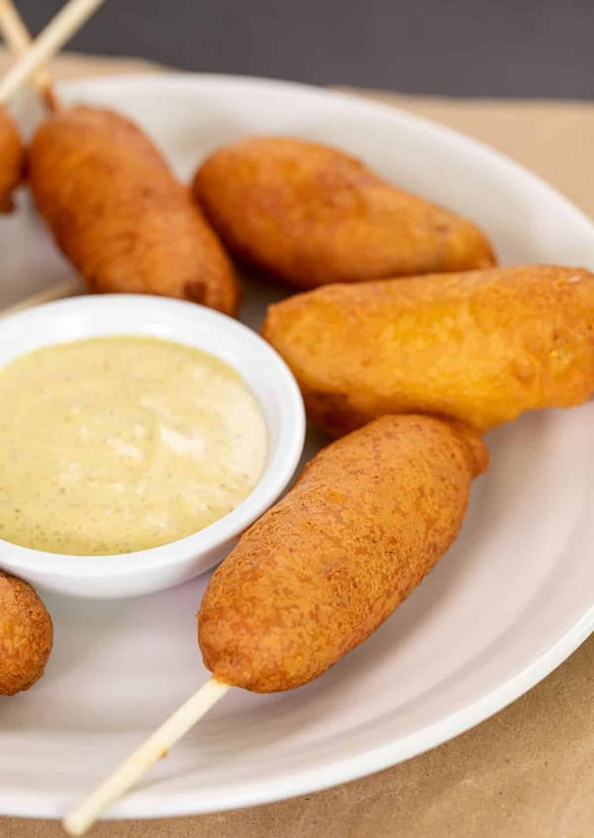 Crunchy gluten-free corn dogs with a bowl of dip on a white tray.