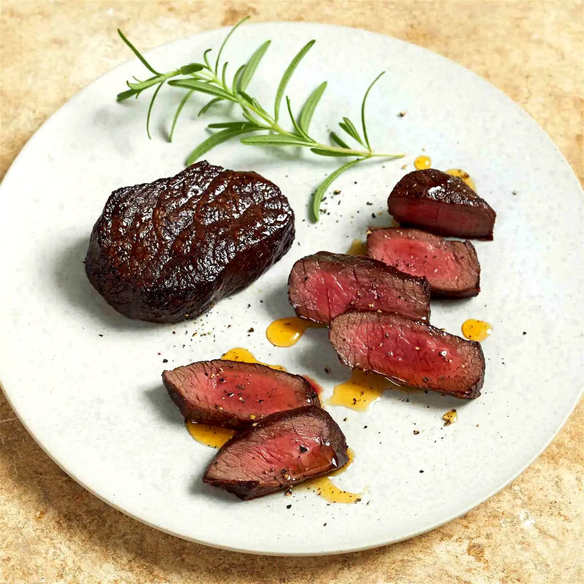 Delicious pan seared elk medallions with honey rosemary sauce on a white plate.