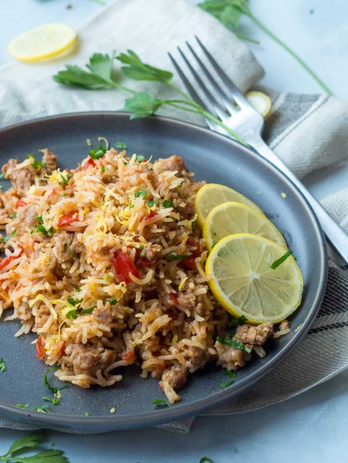 Flavorful sausage rice pot on a gray plate with slices of lemon.