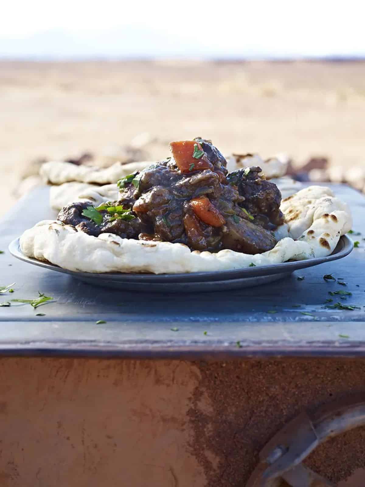 Juicy venison & juniper stew on a black plate.