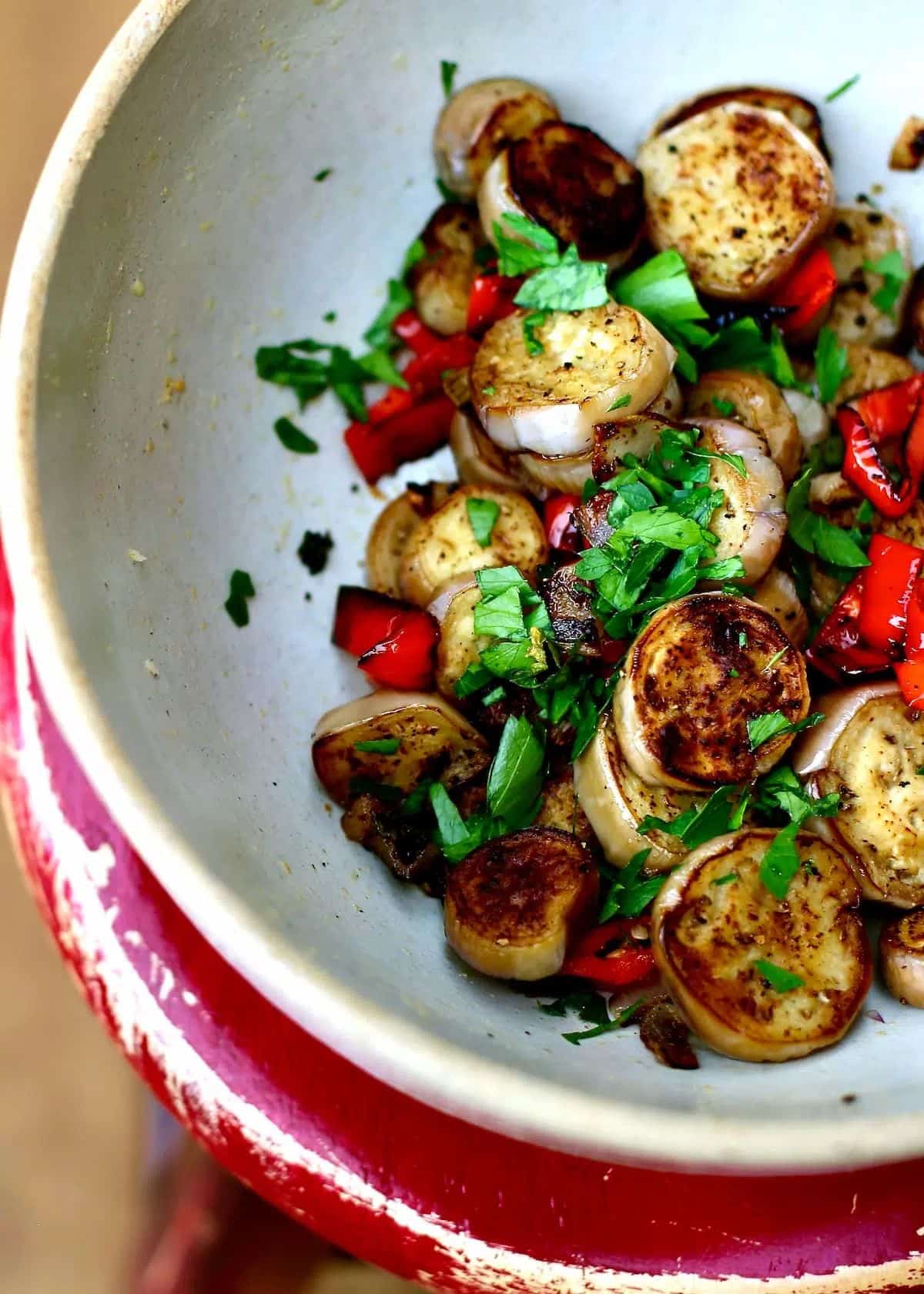 Healthy sliced baby eggplants with anaheim chilis in a white bowl.