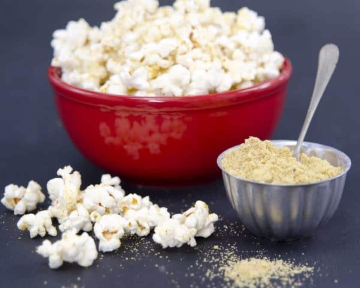 Vegan parmesan in a metal bowl with a bowl of popcorn on a table.