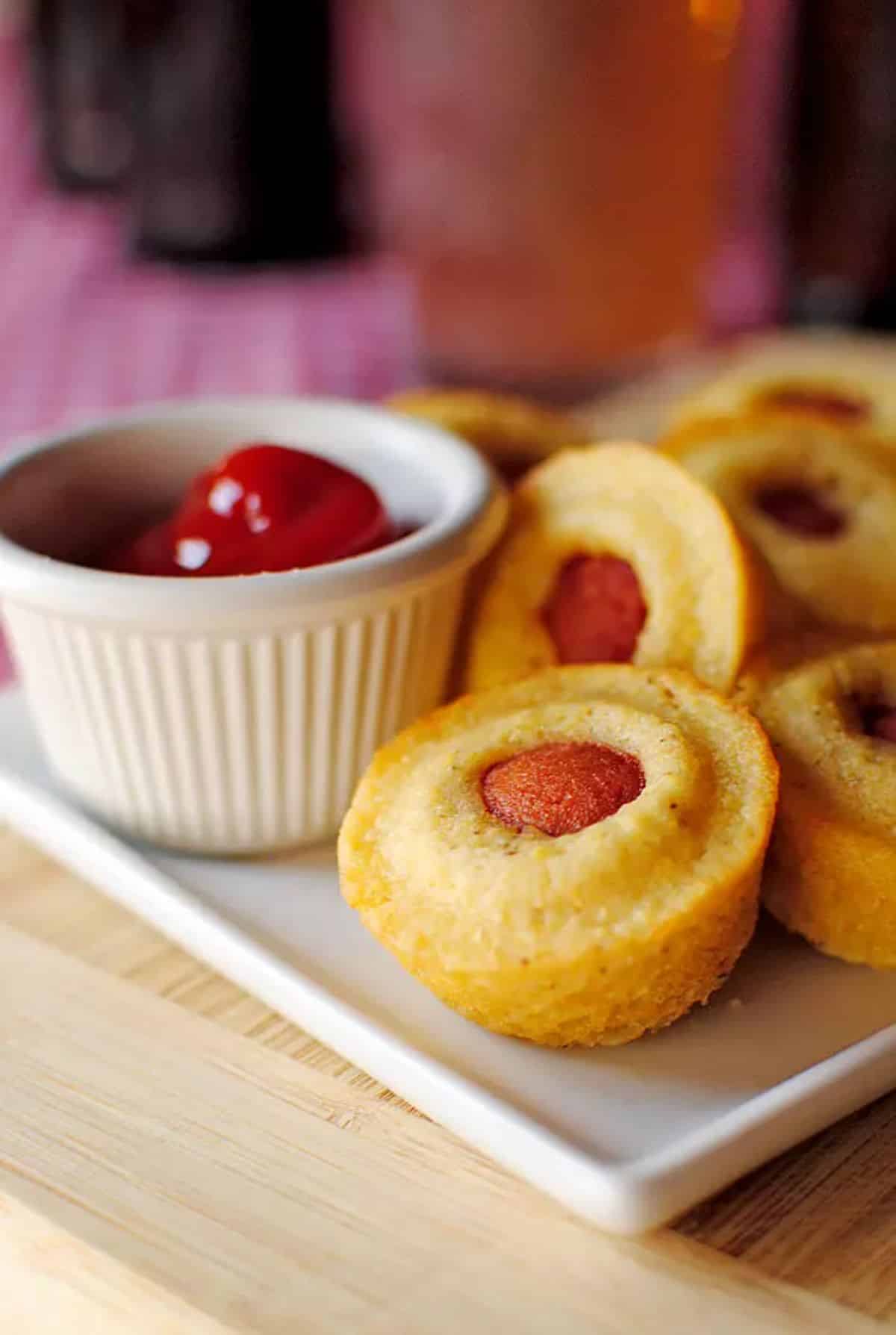 Flavorful mini corn dog muffins with a bowl of dip on a white tray.