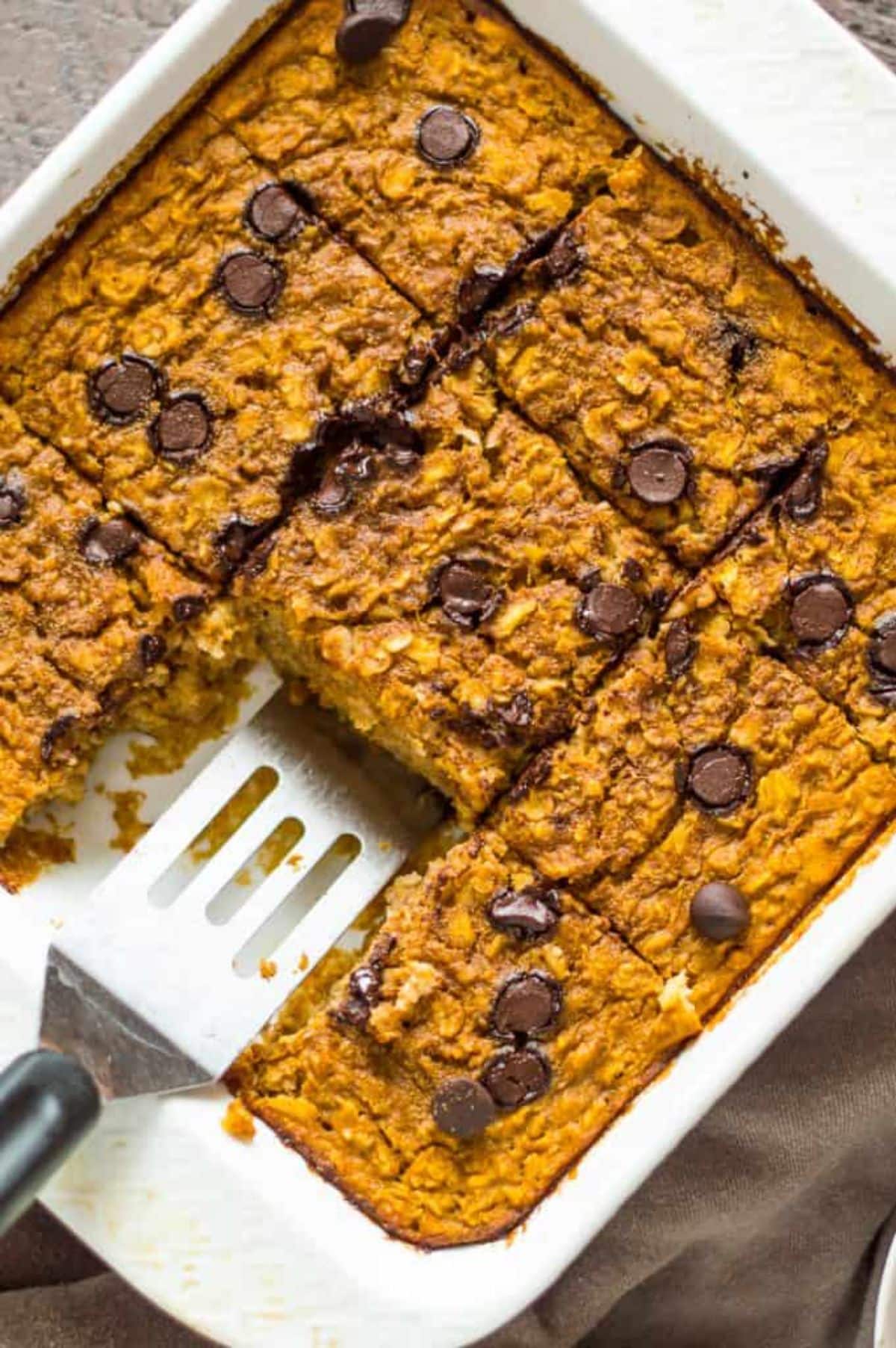 Flavorful pumpkin baked oatmeal in a white casserole with a spatula.