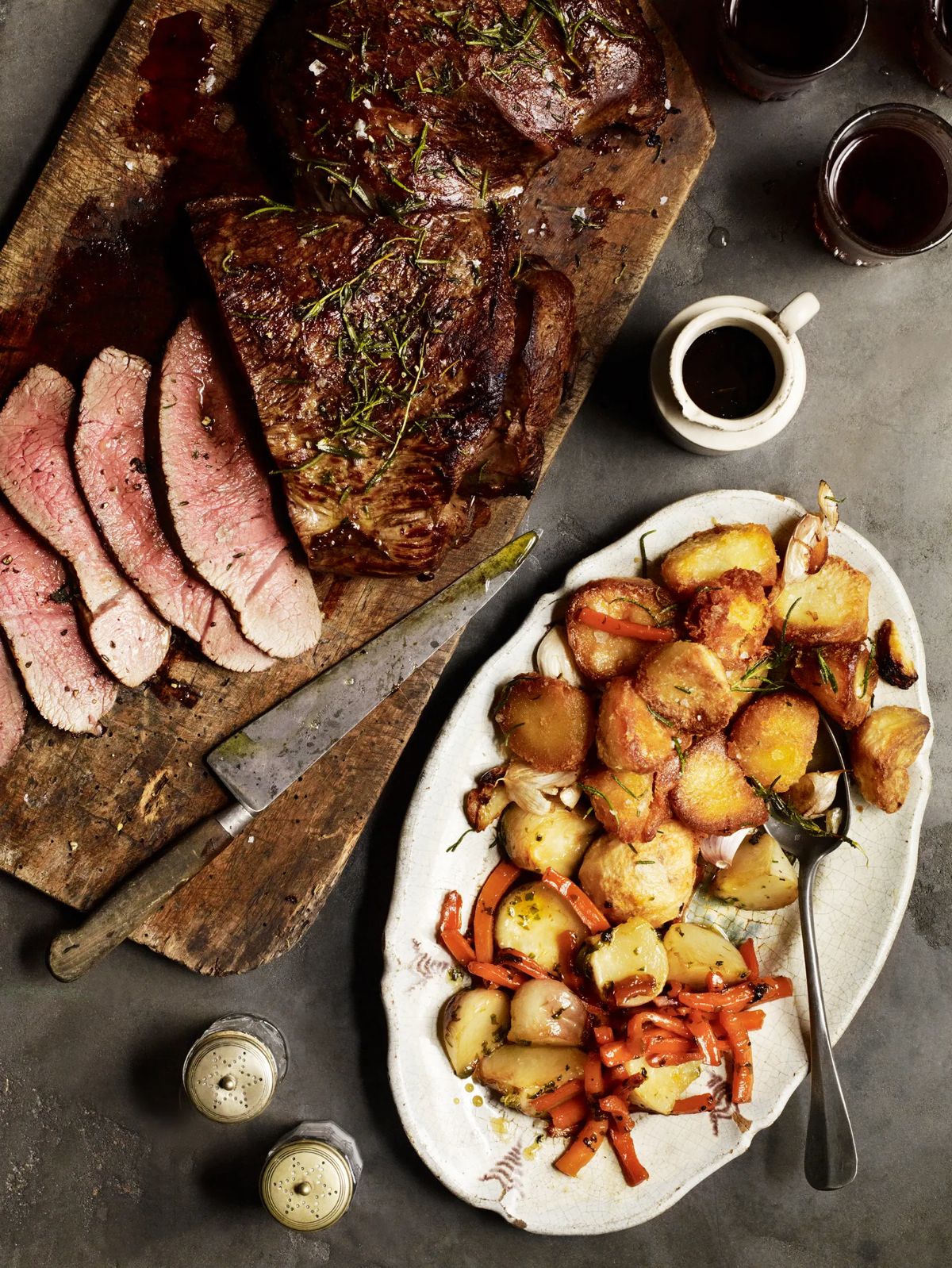 Sliced roast venison on awooden cuttingb board with side dish on a table.