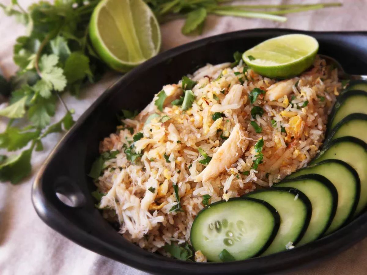 Healthy thai-style crab fried rice with slices of cucumber in a black bowl.