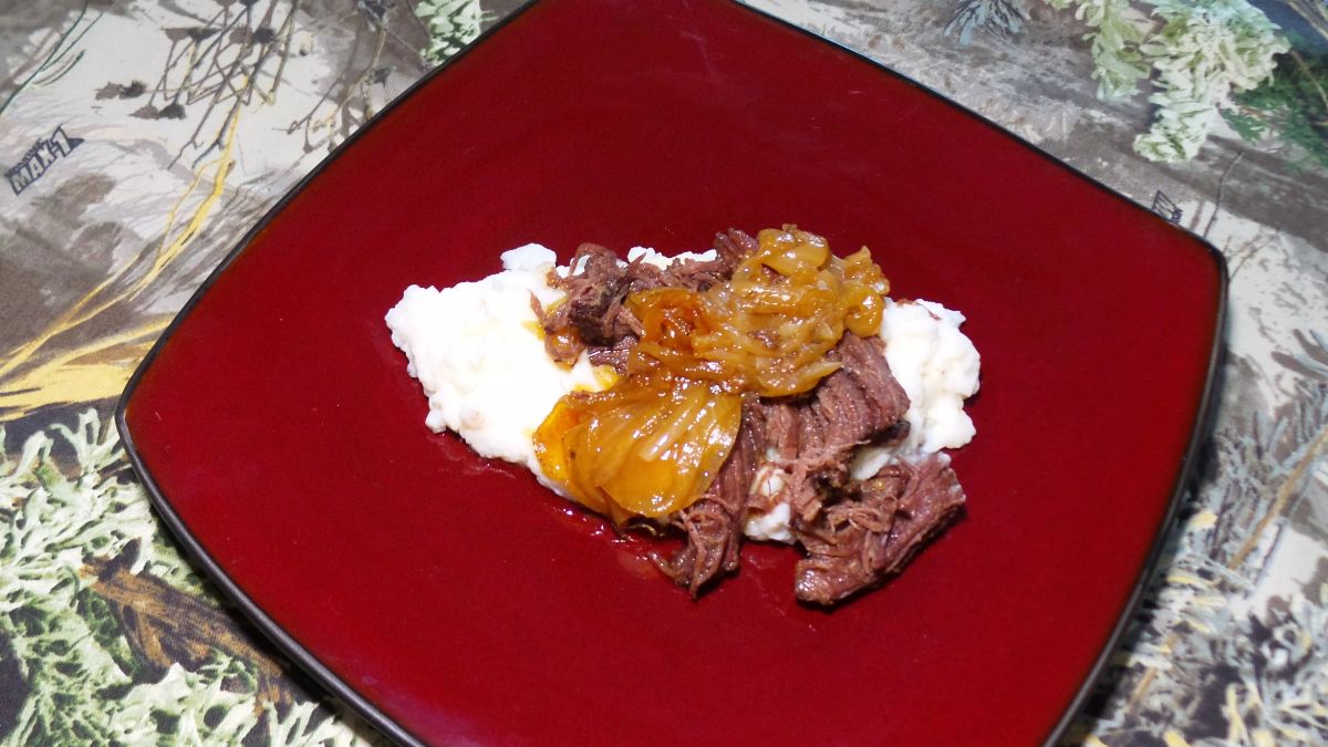 Tasteful beer-brased elk chuck roast with onions on a red plate.