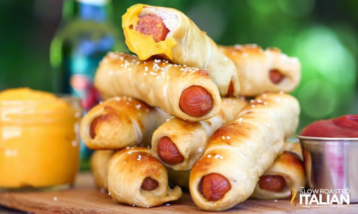 A pile pretzel dogs on a wooden tray.