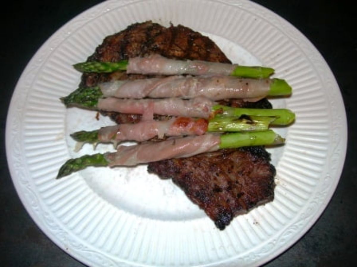 Mouth-watering grilled asparagus wrapped with prosciutto on a white plate.