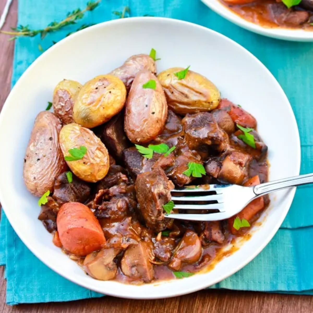 Healthy venison bourguignon in a white bowl with a fork.