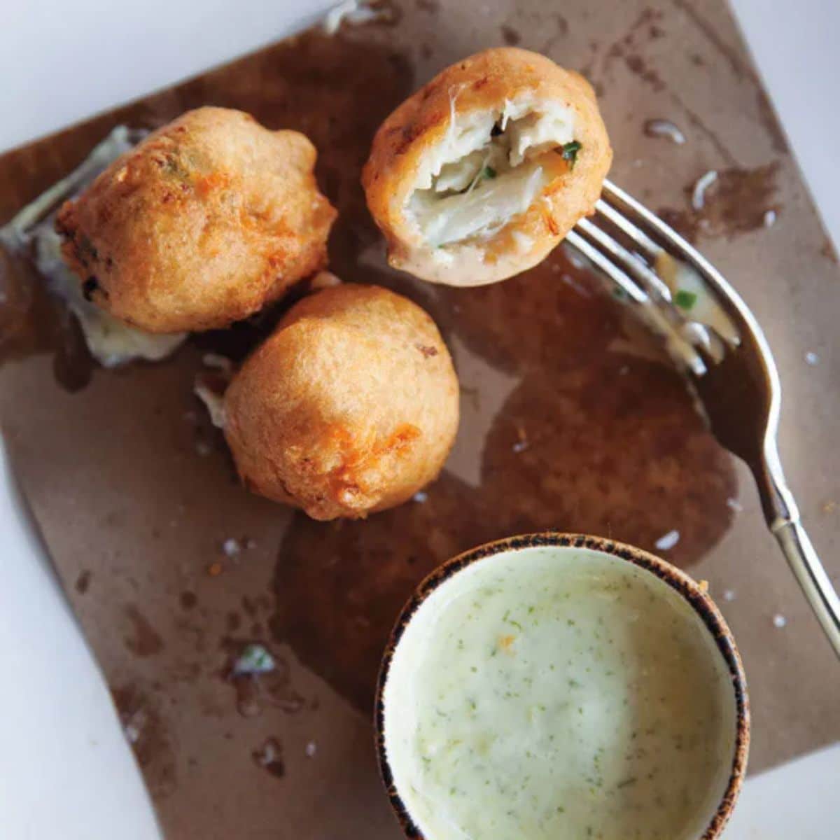 Crunchy blue crab beignets on a tray with a fork and a bowl of dip.