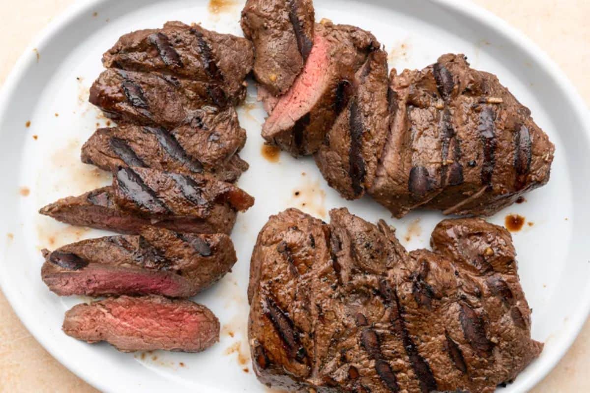 Delicious grilled lemon-garlic elk steaks on a white tray.