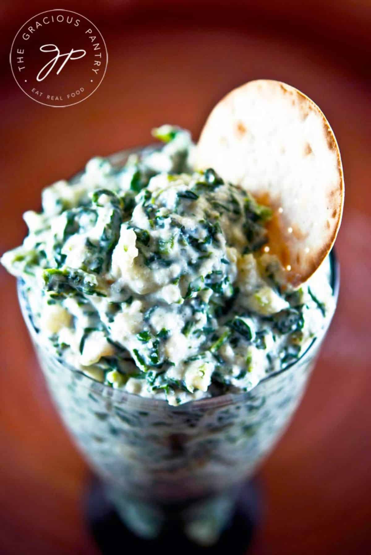 Creamy spinach dip in a glass cup with a cracker.