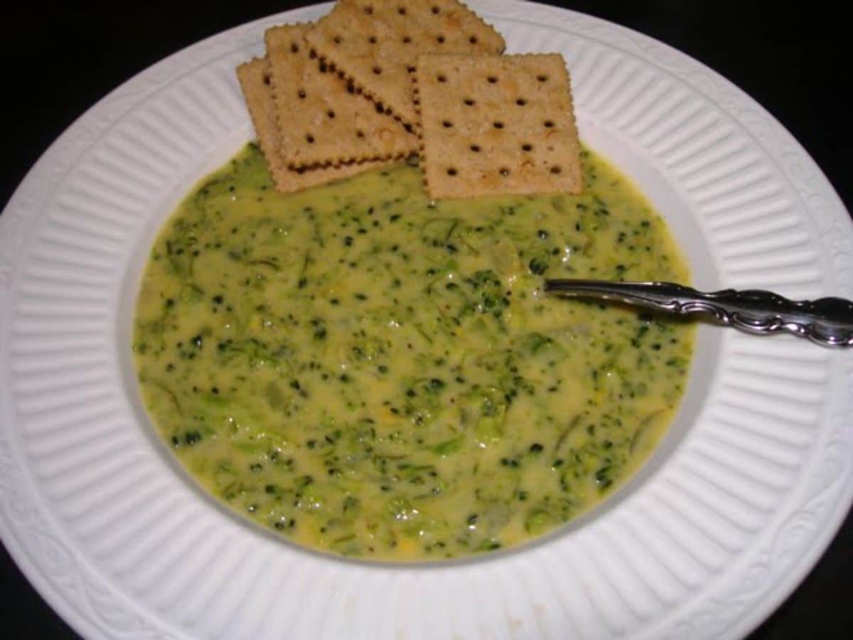 Creamy broccoli cheese soup with crackers and spoon on a white plate.