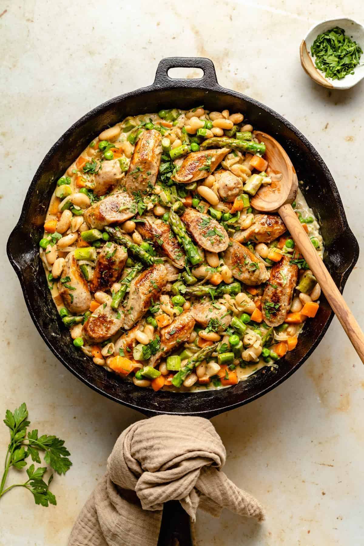 Healthy creamy chicken sausage in a black skillet with a wooden spoon.