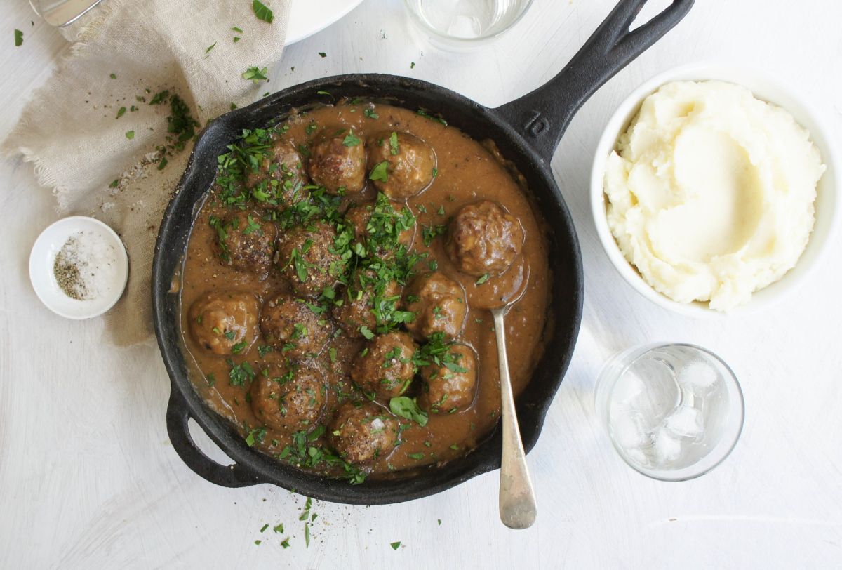 Juicy swedish meatballs in a black skillet with a spoon.